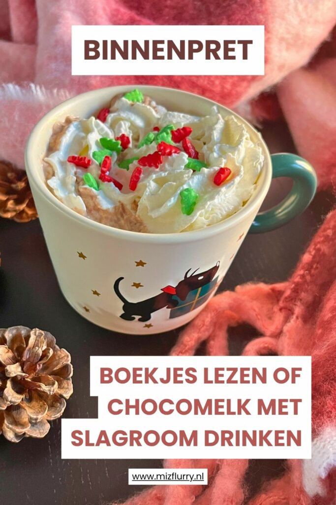Mok warme chocolademelk met slagroom en sprinkles op een tafel met plaid, dennenappels en tekst “Binnenpret – boekjes lezen of chocolademelk met slagroom drinken”