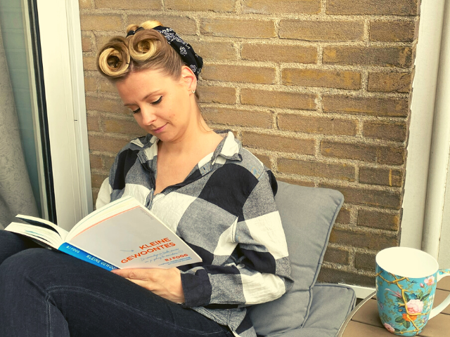 Foto van een moeder die een boek leest op het balkon met een kopje thee