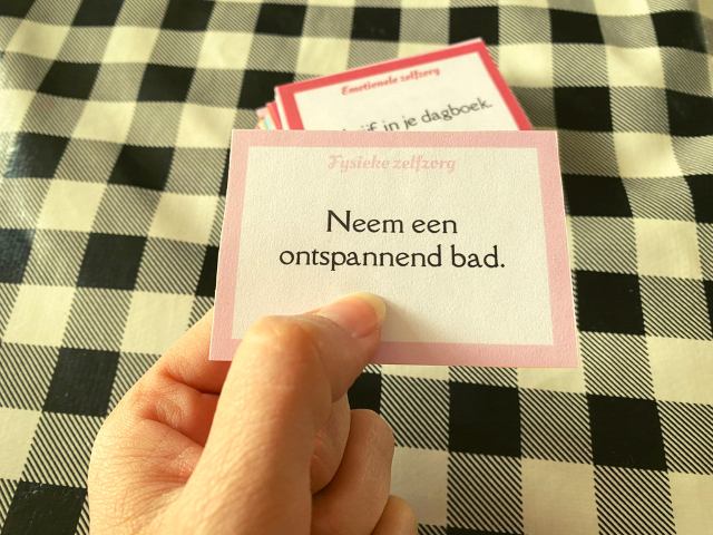 Foto van een zelfhulpkaartje in een hand met de tekst Neem een ontspannend bad.